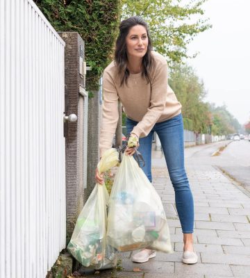 Auf dem Bild sieht man ein Frau die gelbe Säcke für die Abholung durch die Müllabfuhr an die Straße stellt. Nachhaltige Verpackungen und richtiges Entsorgen schützen die Umwelt und verlagern den Earth Overshoot Day nach hinten. 