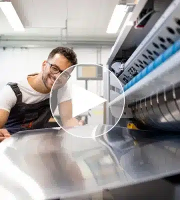 Auszubildender zum Mechatroniker in der Kunststoffindustrie prüft lächelnd eine Metallplatte an einer modernen Produktionsmaschine – in einer zukunftsorientierten technischen Ausbildung.