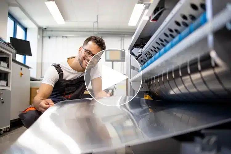 Auszubildender zum Mechatroniker in der Kunststoffindustrie prüft lächelnd eine Metallplatte an einer modernen Produktionsmaschine – in einer zukunftsorientierten technischen Ausbildung.