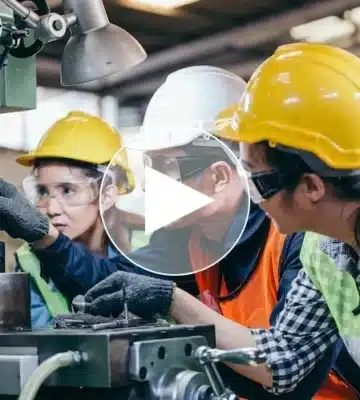 Ausbilder zeigt zwei Auszubildenden zur Werkzeugmechanikerin die präzise Bedienung einer Fräsmaschine in der Produktionshalle – praxisorientierte Lehre in der Kunststoffindustrie.
