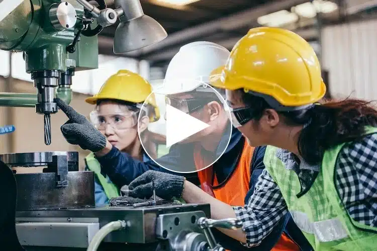 Ausbilder zeigt zwei Auszubildenden zur Werkzeugmechanikerin die präzise Bedienung einer Fräsmaschine in der Produktionshalle – praxisorientierte Lehre in der Kunststoffindustrie.